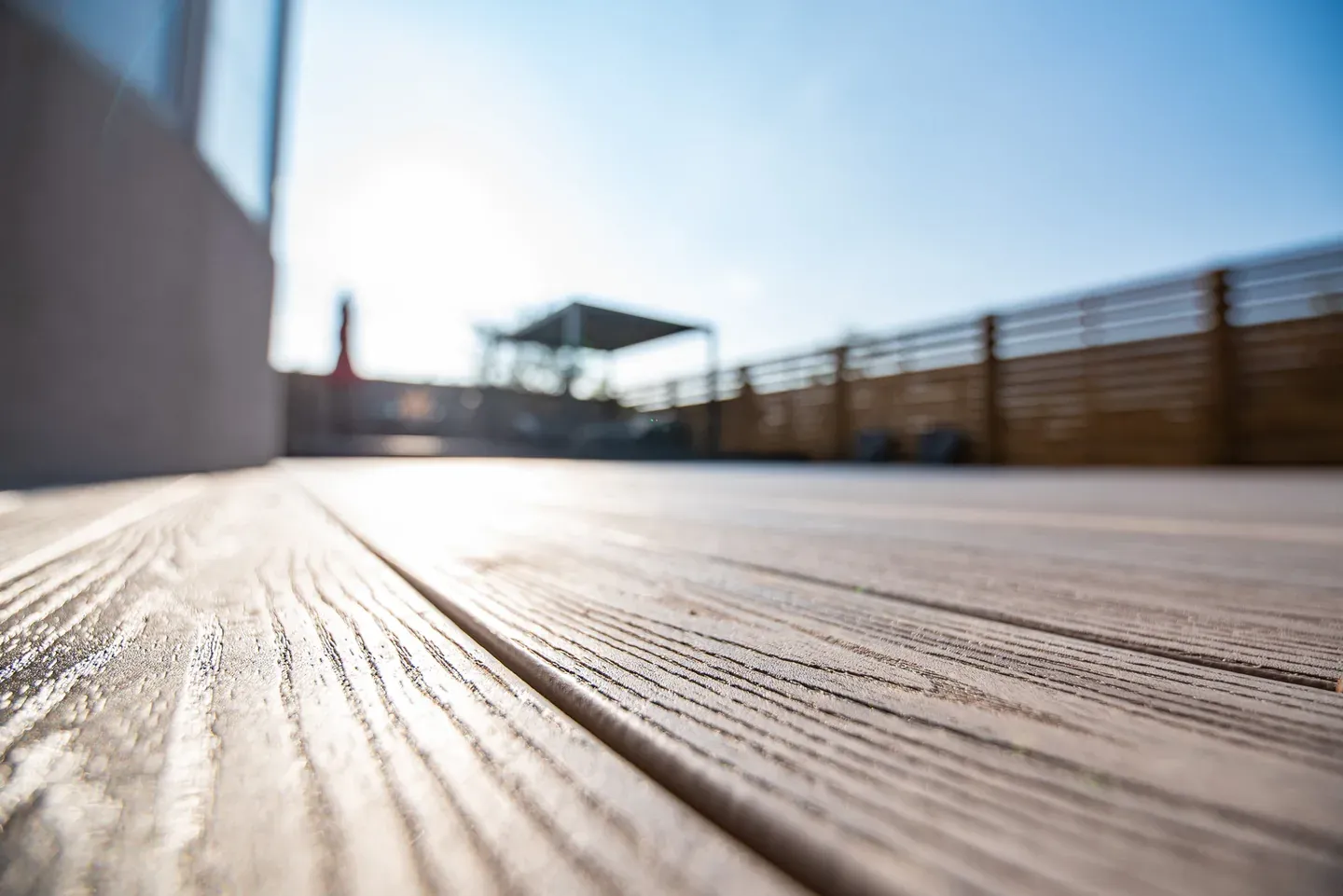 Low-angle close-up of grey composite board grain and the gap between two boards in sunlight.