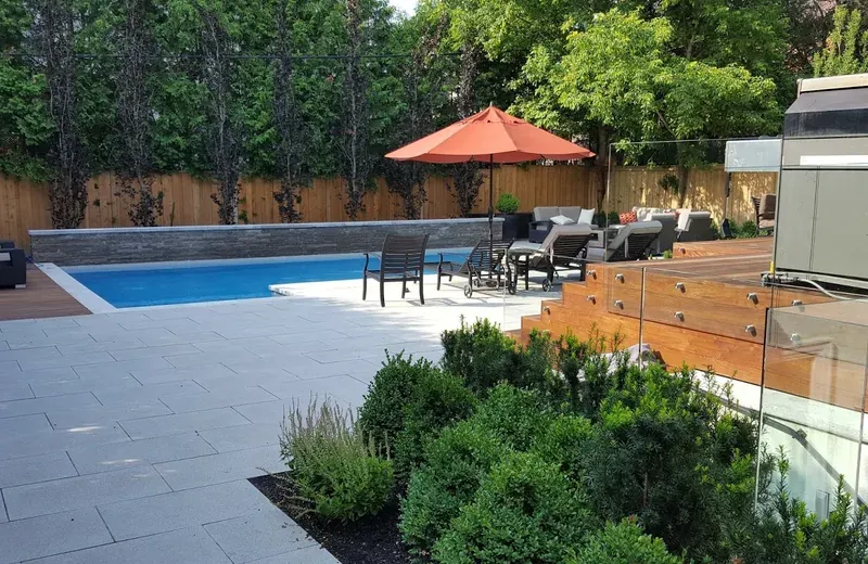 A backyard swimming pool with a raised Ipe hardwood deck and glass railing along its right-hand edge