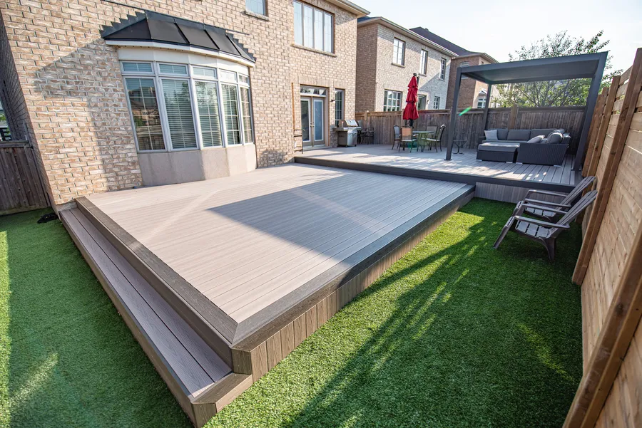 Finished grey deck with a contrasting border, wide steps, a pergola and adjoining lawn