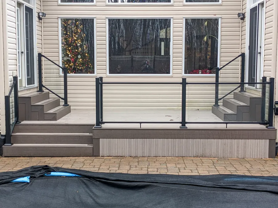 Clear glass railing panels and black posts enclosing a low deck with steps at both ends