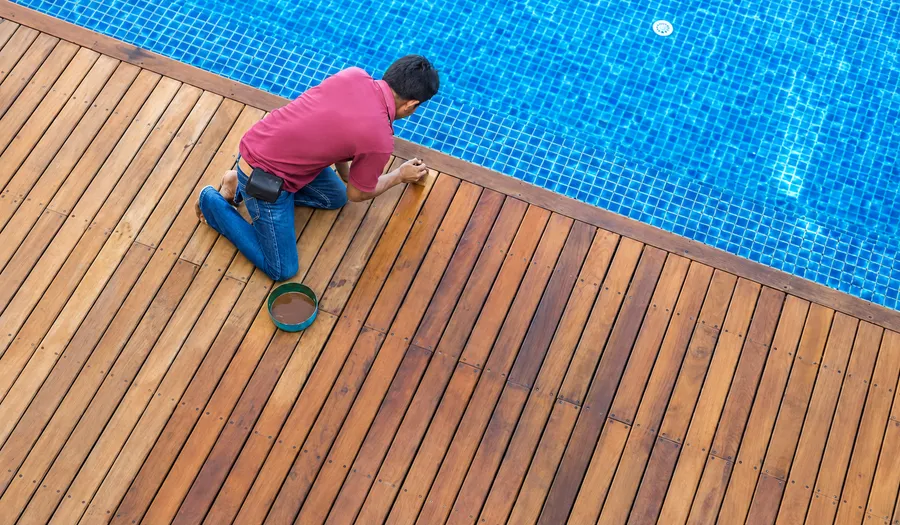 Worker applying finish to brown Ipe deck boards beside a pool