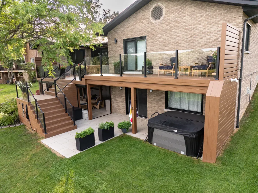 Two-level brown deck with glass guards, an upper dining area and a sheltered patio and hot tub below.
